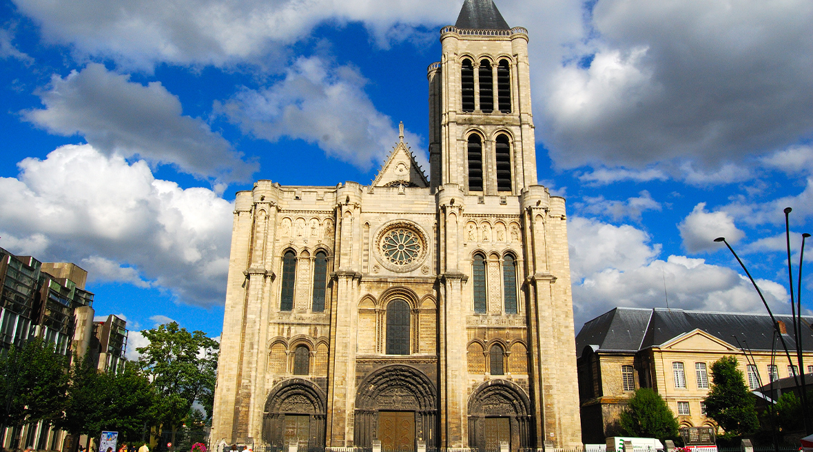 A façade of a Gothic cathedral stands on a main city square. The sky is blue but cloudy